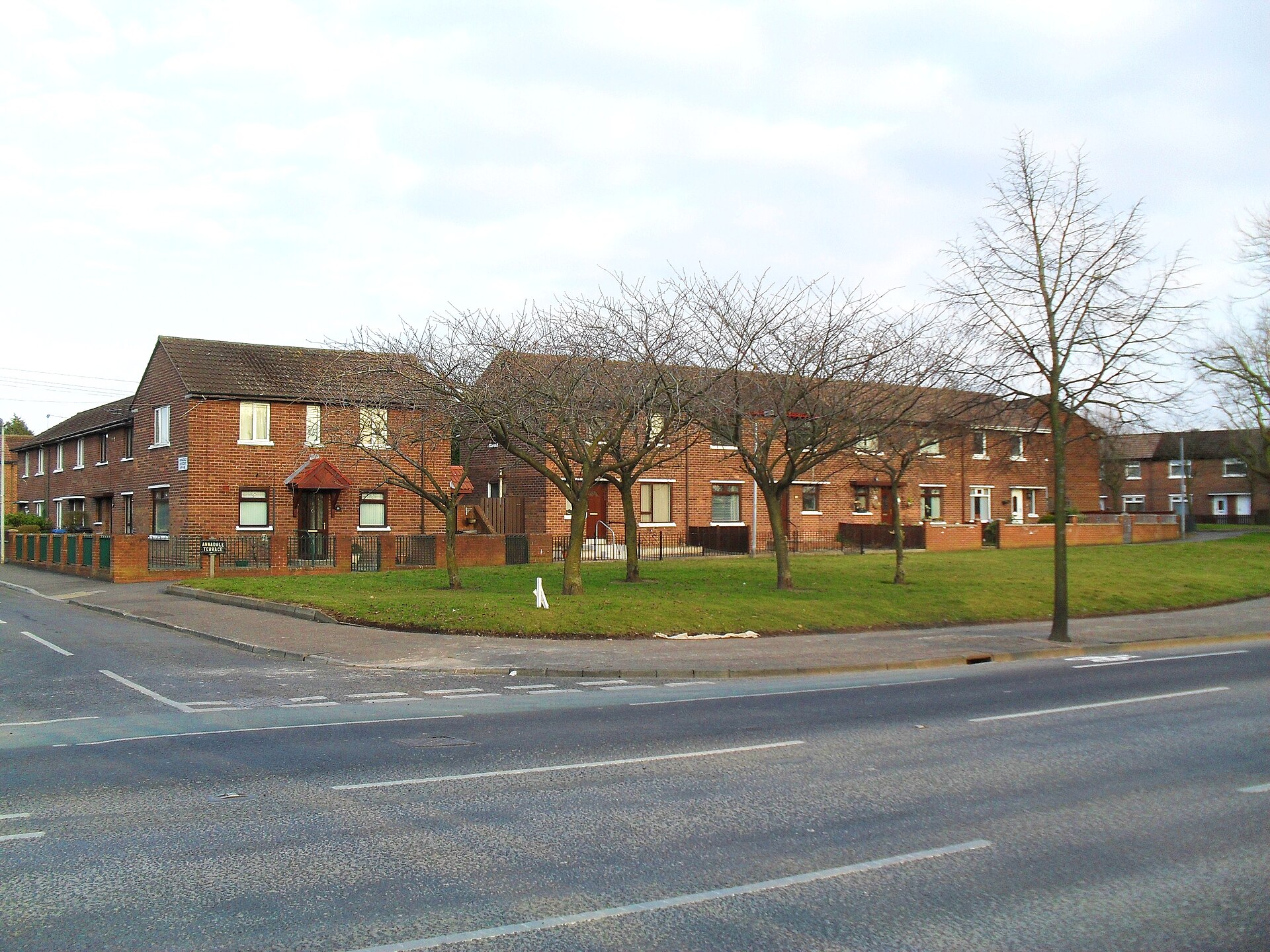 Red-brick terraced houses on a Belfast corner, with bare trees on a green